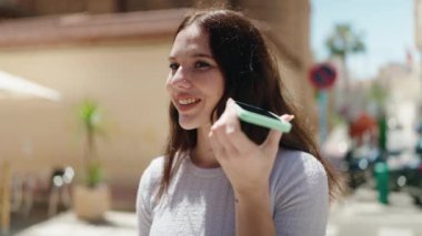 Young woman smiling confident listening audio message by the smartphone at street