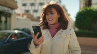 Middle age redhead woman smiling confident having video call at street