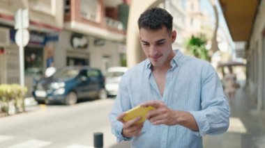 Young hispanic man smiling confident playing video game at street