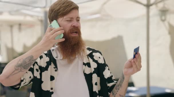 Genç Kızıl Saçlı Adam Elinde Kredi Kartıyla Akıllı Telefondan Konuşuyor — Stok video