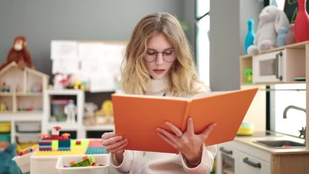 Young Blonde Woman Preschool Teacher Reading Book Relaxed Expression Kindergarten — Stockvideo