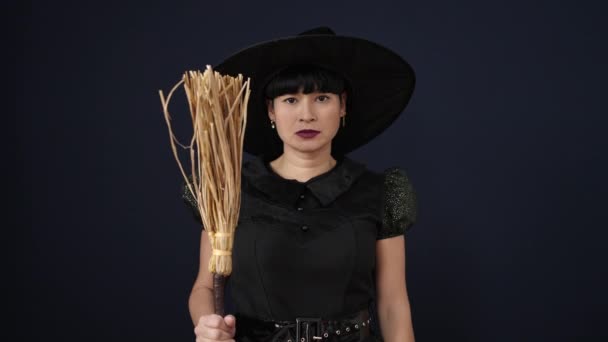 若いです中国の女性身に着けています魔女衣装保持ほうき上の隔離された黒背景 — ストック動画