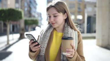 Genç sarışın kadın akıllı telefon kullanıyor. Sokakta kahve içiyor.