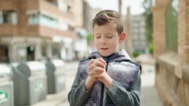 Sarışın çocuk gülerek sokakta dua ediyor.