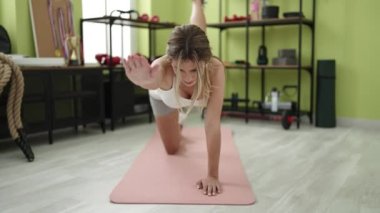 Genç sarışın kadın spor merkezinde yoga minderinde yatıyor.