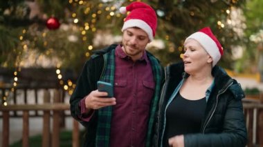 Noel şapkası takan anne ve oğul parkta akıllı telefondan selfie çekiyor.