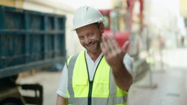 Orta yaşlı mimar kendinden emin gülümsüyor. Sokakta el kol hareketi yapıyor.