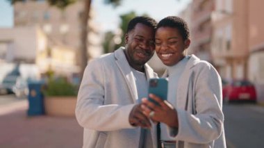 Afro-Amerikalı çift sokakta akıllı telefon kullanarak gülümsüyor.