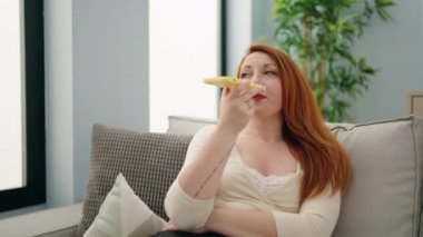 Young redhead woman talking on the smartphone sitting on sofa at home