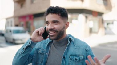 Genç Arap adam gülümsüyor, kendinden emin bir şekilde caddedeki akıllı telefondan konuşuyor.