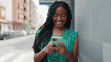 Afro-Amerikalı kadın sokakta akıllı telefon kullanarak kendine güveniyor.