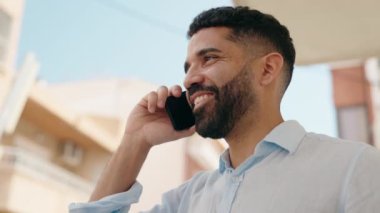 Genç Arap adam gülümsüyor, kendinden emin bir şekilde caddedeki akıllı telefondan konuşuyor.