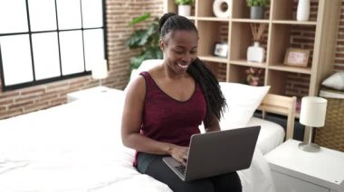 African woman using laptop sitting on bed at bedroom