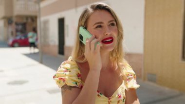 Genç, güzel, İspanyol bir kadın gülümsüyor ve caddede akıllı telefondan konuşuyor.