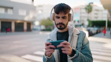 Young hispanic man smiling confident playing video game at street