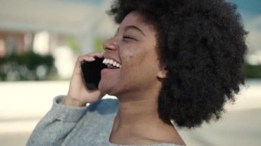 Afro-Amerikalı kadın gülümsüyor. Parktaki akıllı telefondan konuşuyor.