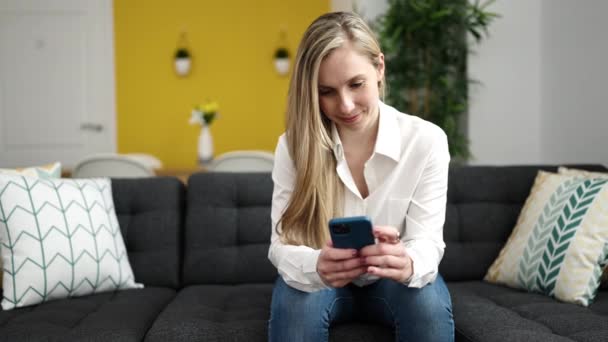 Junge Blonde Frau Sitzt Mit Smartphone Hause Auf Sofa — Stockvideo
