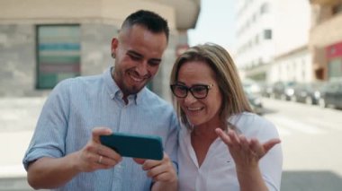Kadın, erkek, anne ve kız caddede akıllı telefondan video izliyorlar.