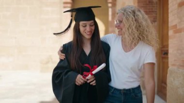 İki kadın anne ve mezun kız kampüs üniversitesinde yürürken birbirlerine sarılıyorlar.