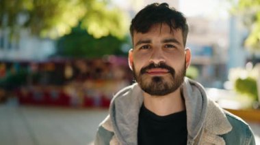 Young hispanic man standing with serious expression at park