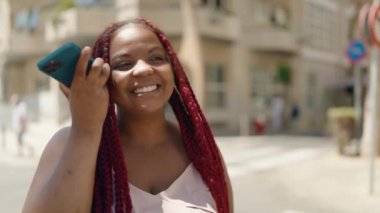 Afro-Amerikalı kadın gülümsüyor. Caddedeki akıllı telefondan kendine güvenen sesli mesaj dinliyor.