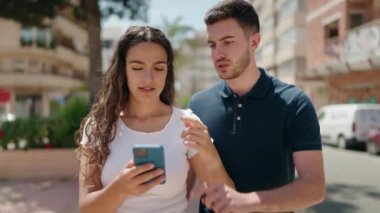 Genç İspanyol çift sokakta akıllı telefon kullanarak gülümsüyor.