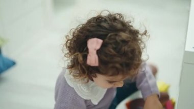 Adorable hispanic girl playing with construction blocks standing at kindergarten