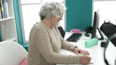 Orta yaşlı bir kadın, gri saçlı bir öğretmen, not defterine yazıyor. Üniversite sınıfında sırt ağrısı çekiyor.