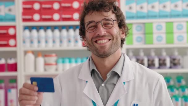 Fiatal Spanyol Férfi Gyógyszerész Mosolyog Magabiztos Gazdaság Hitelkártya Gyógyszertárban — Stock videók