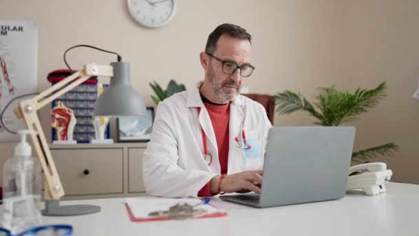 Middle Age Man Doctor Using Laptop Writing Document Clinic — Vídeo de stock