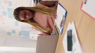 African american woman business worker using laptop writing on document vertical video at office