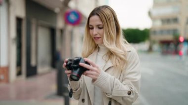 Young blonde woman smiling confident using professional camera at street
