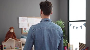 Young hispanic man preschool teacher smiling confident standing with arms crossed gesture at kindergarten