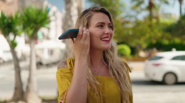 Caddedeki akıllı telefondan kendine güveni tam bir sesli mesaj dinleyen genç bir kadın.