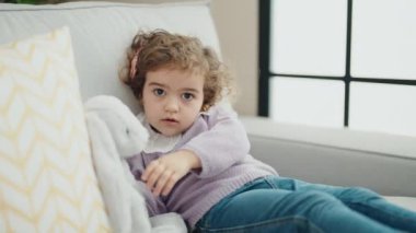 Adorable hispanic girl sitting on sofa with rabbit doll at home