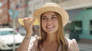 Yaz şapkası takan genç bir turist sokakta akıllı telefondan sesli mesaj dinliyor.