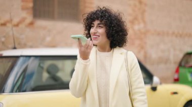 Gülümseyen genç bir kadın caddedeki akıllı telefondan konuşuyor.