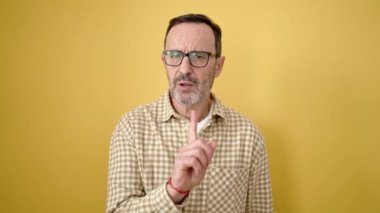 Orta yaşlı bir adam öfkeli bir ifadeyle dikiliyor. İzole edilmiş sarı arka planda parmağını hareket ettirmiyor.