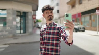 Genç İspanyol adam gülümsüyor. Sokakta akıllı telefonun yanında özçekim yapıyor.