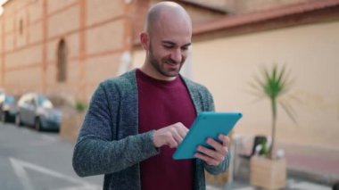 Young bald man smiling confident using touchpad at street