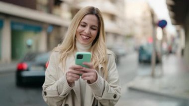 Sokakta akıllı telefon kullanan, kendine güvenen genç sarışın kadın.