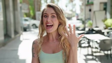 Genç sarışın kadın parmağıyla kahve dükkanının terasına işaret ediyor.