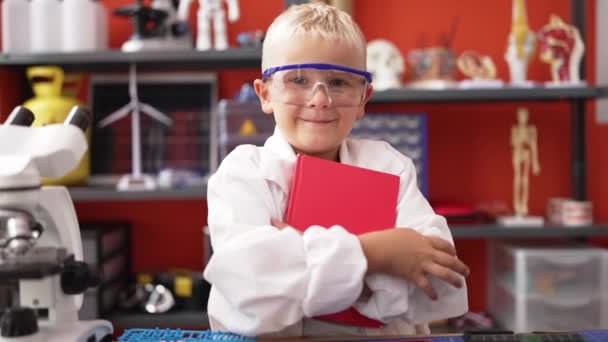 可爱的蹒跚学步的科学家微笑着 自信地拥抱在课堂上的书本 — 图库视频影像