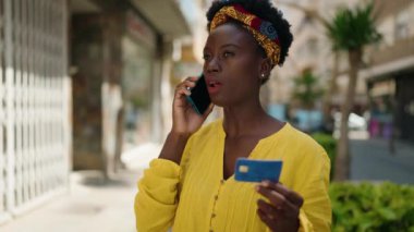 Genç Afrikalı Amerikalı kadın akıllı telefonla konuşuyor ve sokakta kredi kartı kullanıyor.