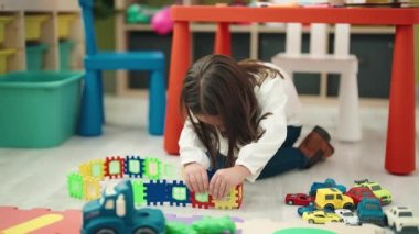 Adorable hispanic girl playing with construction blocks sitting on floor at kindergarten