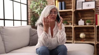 Middle age grey-haired woman worried talking on the smartphone at home