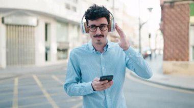 Genç İspanyol adam kendinden emin bir şekilde gülümsüyor müzik dinliyor ve sokakta dans ediyor