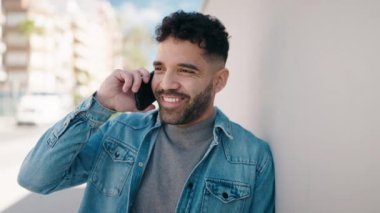 Genç Arap adam gülümsüyor, kendinden emin bir şekilde caddedeki akıllı telefondan konuşuyor.