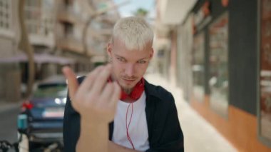 Genç, beyaz bir adam gülümsüyor. Kendine güveniyor. Sokakta bir jest yapıyor.