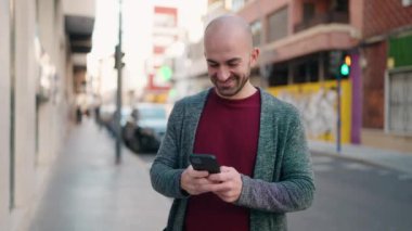 Sokakta akıllı telefon kullanarak kendine güvenen genç kel adam.